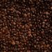 Sacos de café empilhados em armazém portuário, com grãos expostos e luz natural, remetendo à exportação.
