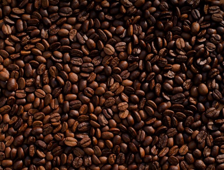 Sacos de café empilhados em armazém portuário, com grãos expostos e luz natural, remetendo à exportação.